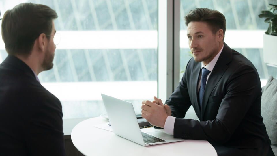 Concentrated confident male hr manager holding interview with young job seeker in modern office. Focused pleasant employer listening to candidate self presentation during one on one meeting.