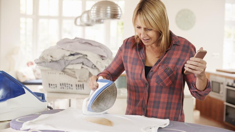 Distracted middle aged woman burns t shirt while ironing