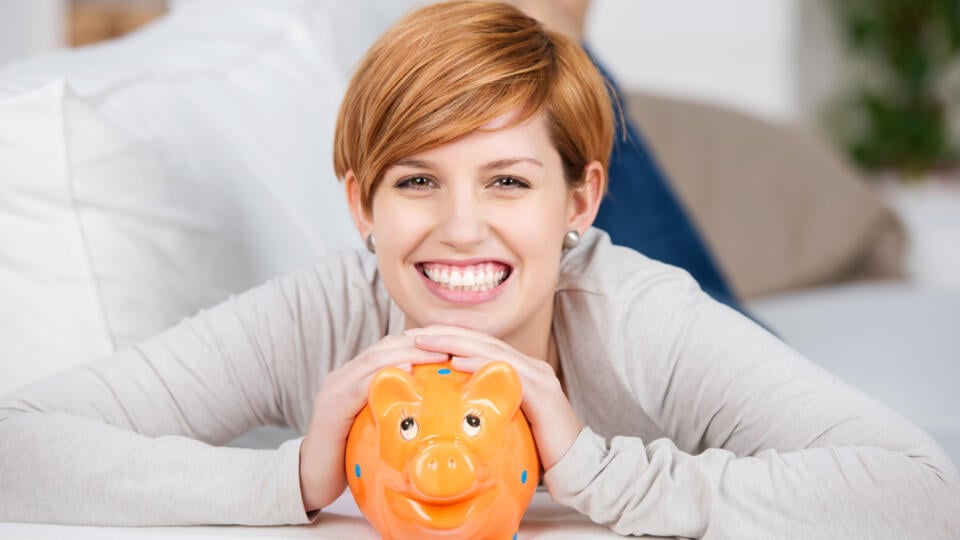 Portrait,Of,Cheerful,Woman,With,Piggy,Bank,While,Lying,On