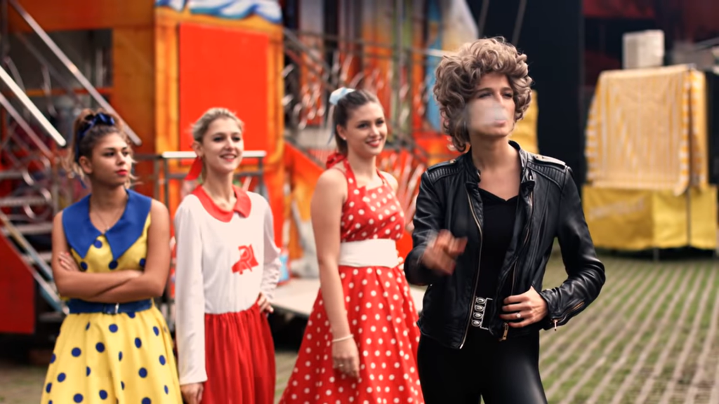Odrazu sa vo videoklipe objavila aj Katarína Saganová s parochňou na hlave. Mladej Olivii Newton John akoby z oka vypadla.