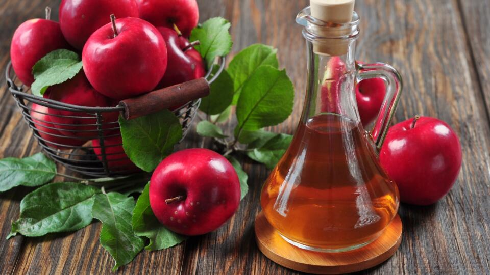 A bottle of apple cider vinegar and a bucket of apples