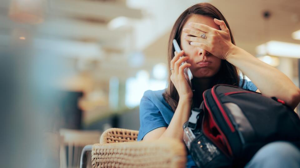 Unhappy,Woman,Talking,On,The,Phone,Waiting,In,An,Airport