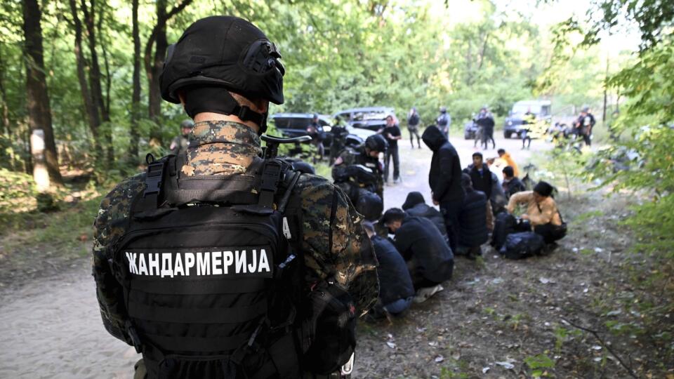 Srbský policajt stráži zadržaných migrantov, ktorí sedia na zemi na neznámom mieste v blízkosti hraníc s Maďarskom v utorok 12. septembra 2023.