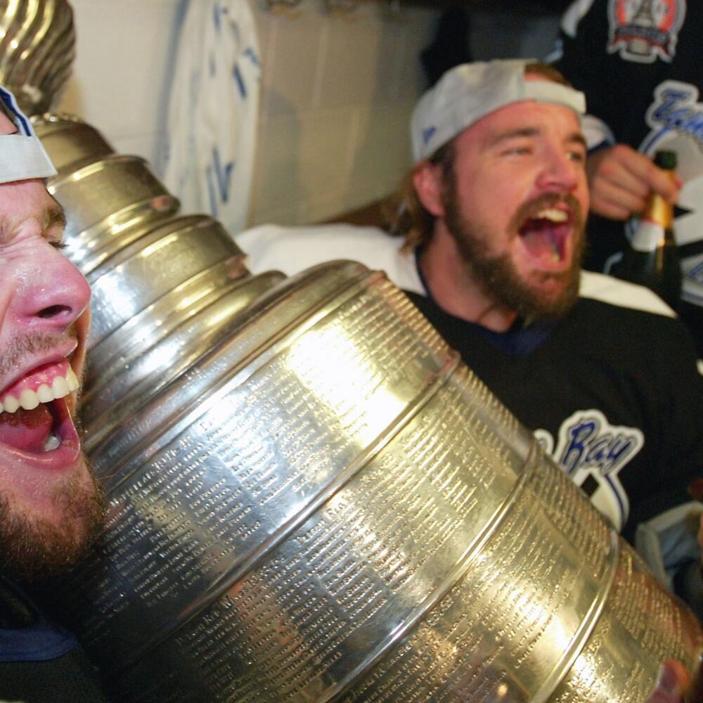 TAMPA, FL - JUNE 7: (L-R) Martin Cibak #8 John Grahame #47 and Stan Neckar #2 of the Tampa Bay Lightning celebrate with the Stanley Cup in the locker room after defeating the Calgary Flames in game seven of the NHL Stanley Cup Finals on June 7, 2004 at the St. Pete Times Forum in Tampa, Florida. The Lightning won the Stanley cup by defeating the Flames 2-1. (Photo by Elsa/Getty Images)