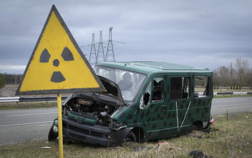 Značka upozorňujúca na nebezpečnú úroveň radiácie stoji pri poškodenom aute s písmenom V, znakom ruskej armády, neďaleko jadrovej elektrárne v Černobyle v sobotu 16. apríla 2022.