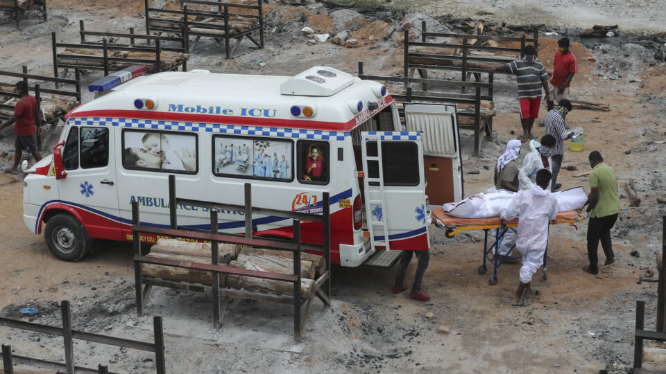 Zdravotný personál vykladá zo sanitky telo obete ochorenia COVID-19, ktoré spopolnia v provizórnom krematóriu v žulovom kameňolome na okraji indického Bengalúru.