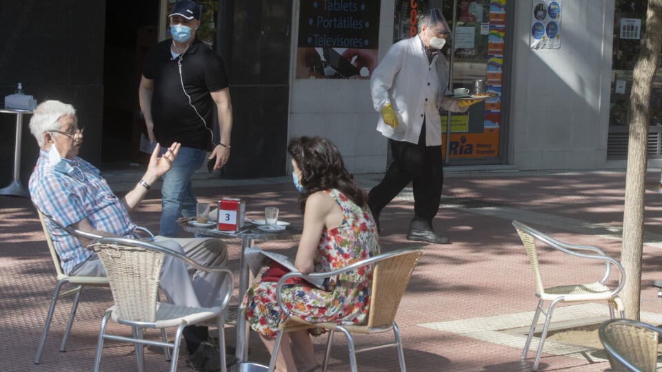 Čašník s ochranným rúškom a rukavicami kráča s podnosom na barovú terasu v Madride.