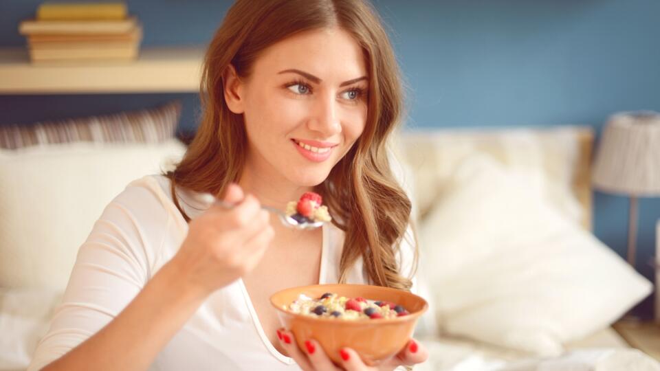 woman in pajamas in bedroom eating muesli with berries