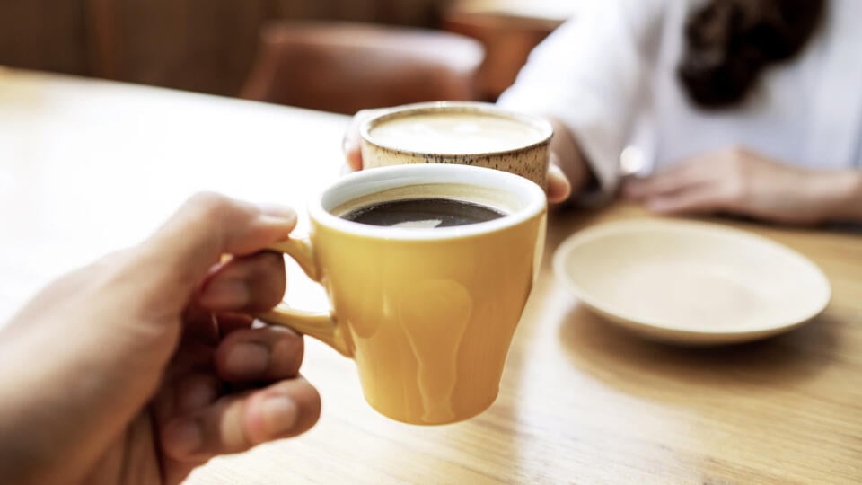 Closeup image of a young couple people clinking coffee cups together in cafe