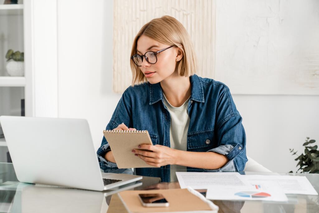 Young,Woman,Taking,Notes,Using,Laptop,For,Remote,Studies,At