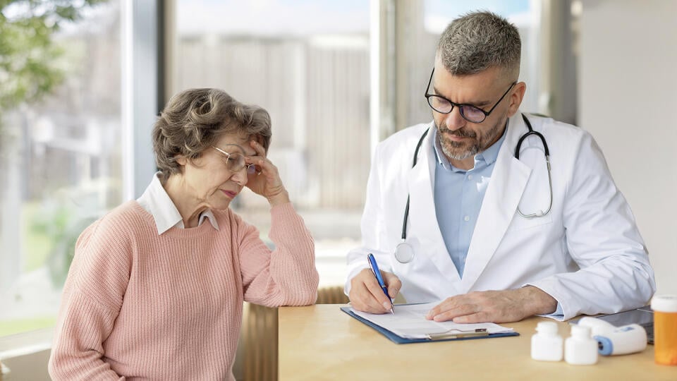 Sad serious old woman listening to male doctor at meeting in hospital, therapist physician consulting elderly patient about disease, treatment