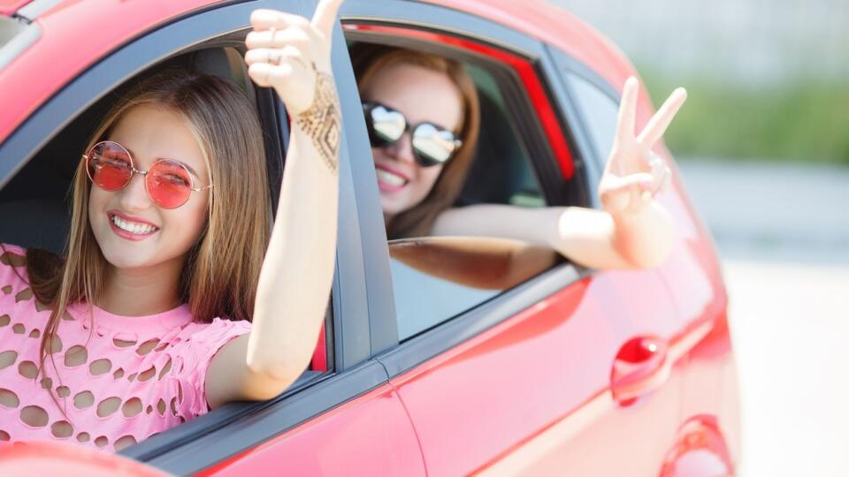 Two happy young girlfriends traveling in the car. Two beautiful young girl with a sweet smile, sun glasses, travel in a pink car in the summer, opening the car window showing thumbs up sign of victory and joy., Image: 255080940, License: Royalty-free, Restrictions: , Model Release: yes, Credit line: Profimedia, Stock Budget