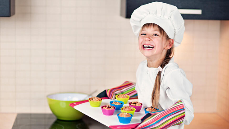 Happy little girl chef with freshly cooked cupcakes.