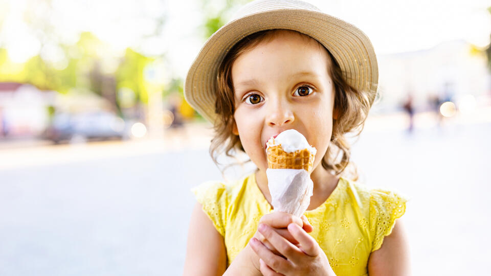 a child eats ice cream in the summer when it's hot outside. Ice cream in a waffle cone. A happy and contented child in a hat and dress.