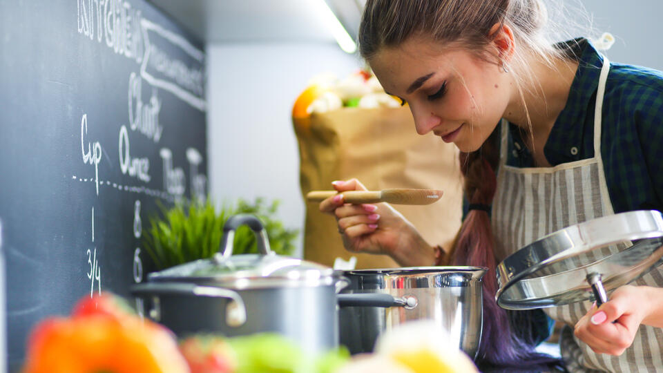 Young,Woman,Standing,By,The,Stove,In,The,Kitchen,.