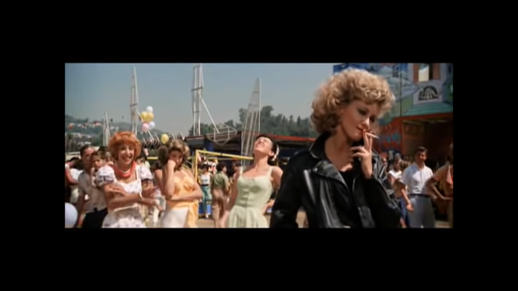 Odrazu sa vo videoklipe objavila aj Katarína Saganová s parochňou na hlave. Mladej Olivii Newton John akoby z oka vypadla.