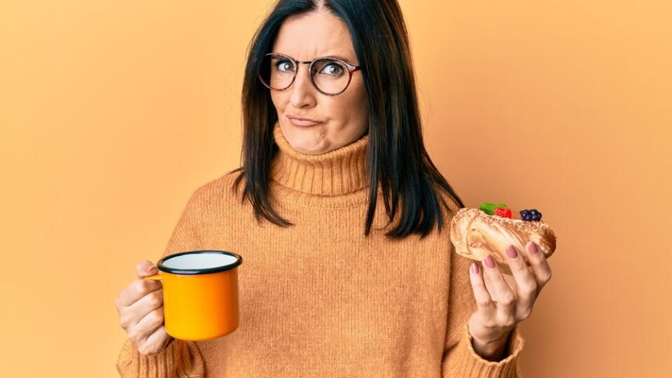 Middle,Age,Brunette,Woman,Eating,Pastry,And,Drinking,Coffee,Skeptic