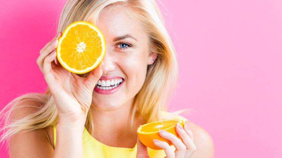 Happy,Young,Woman,Holding,Oranges,Halves,On,A,Pink,Background