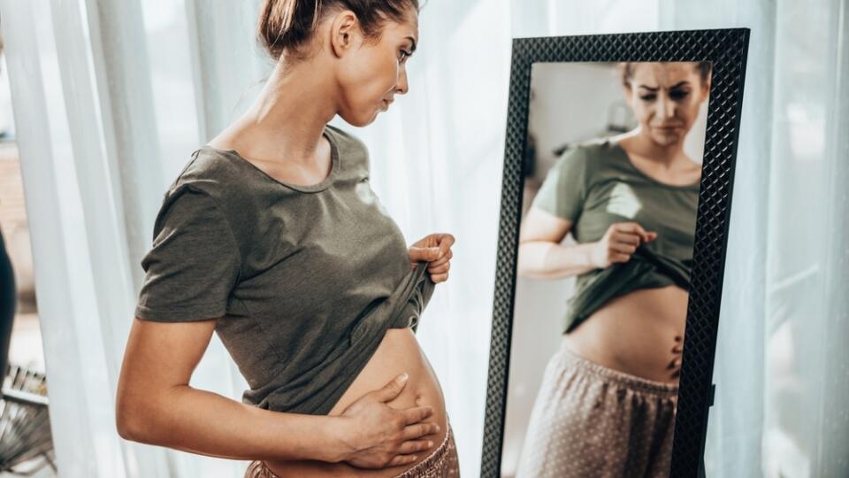 Unhappy,Woman,Standing,In,Front,Of,A,Mirror,And,Holding