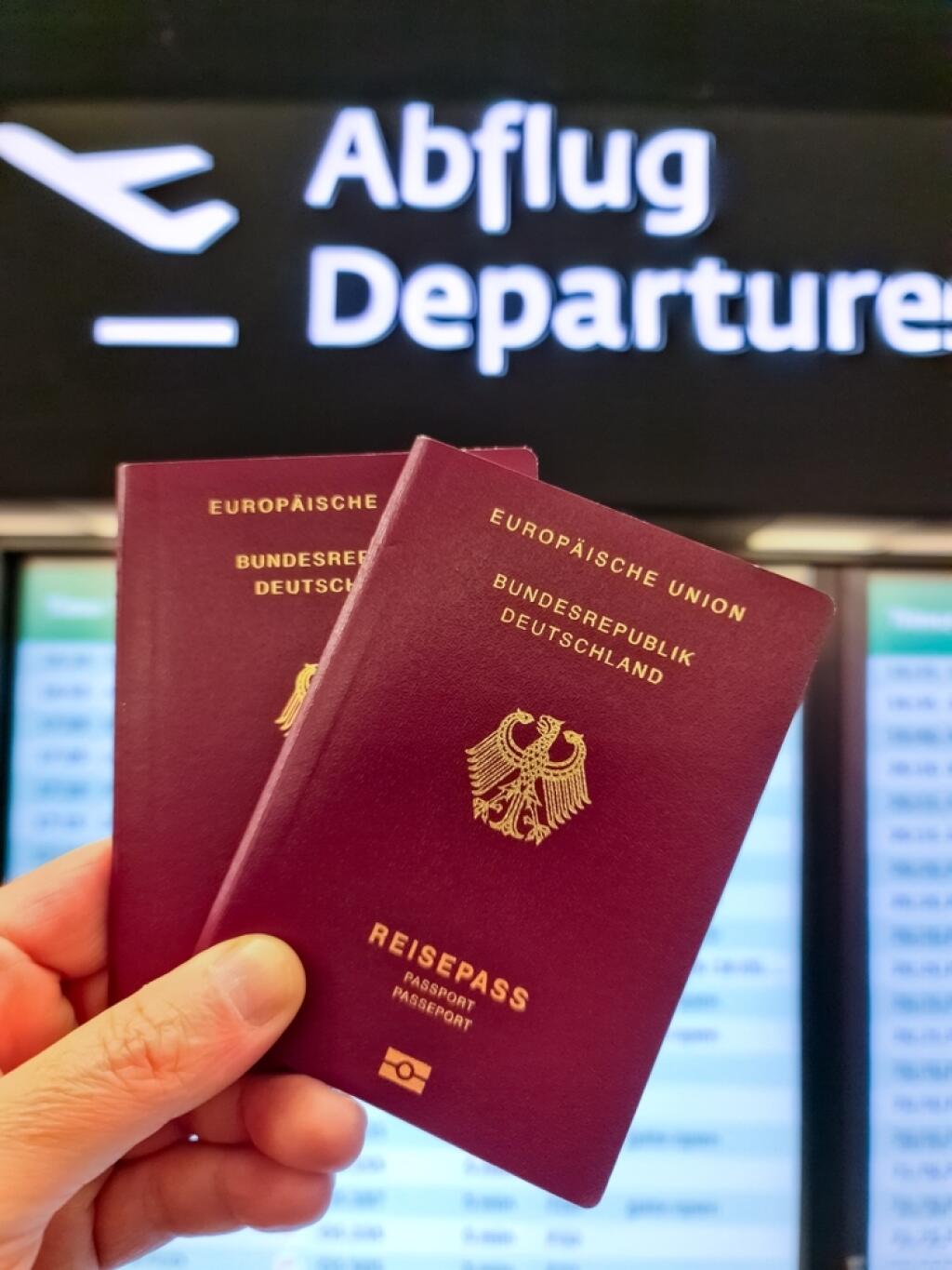 A hand holds two German passports in front of a soft travel airport background on vacation