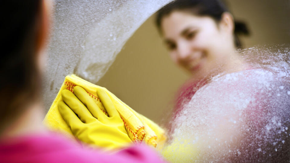 Woman smiling cleaning a mirror blurred background, soft focus intended to create interest in subject matter. 