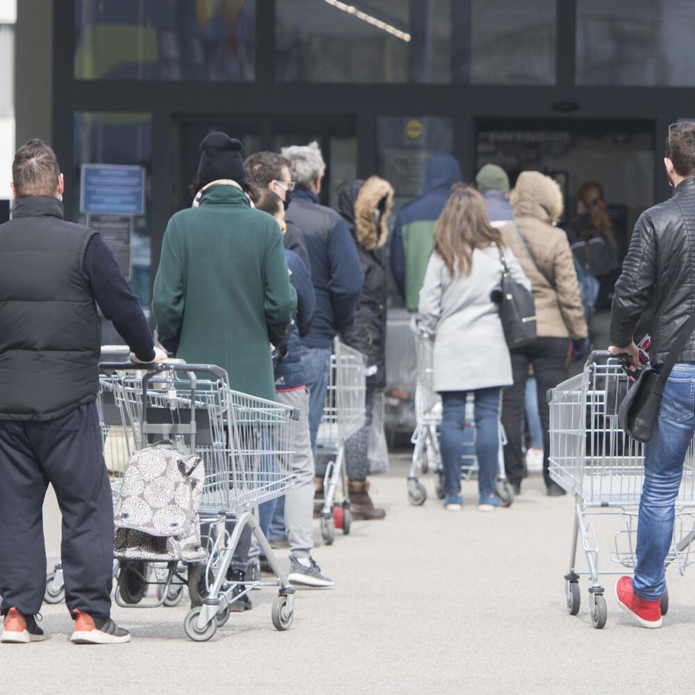 Čakajúci ľudia stoja v rade pred obchodom. Tie regulujú vstupy kvôli vírusu Covid-19.
