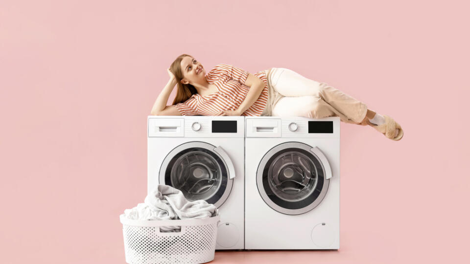 Pretty young woman lying on washing machines against pink background