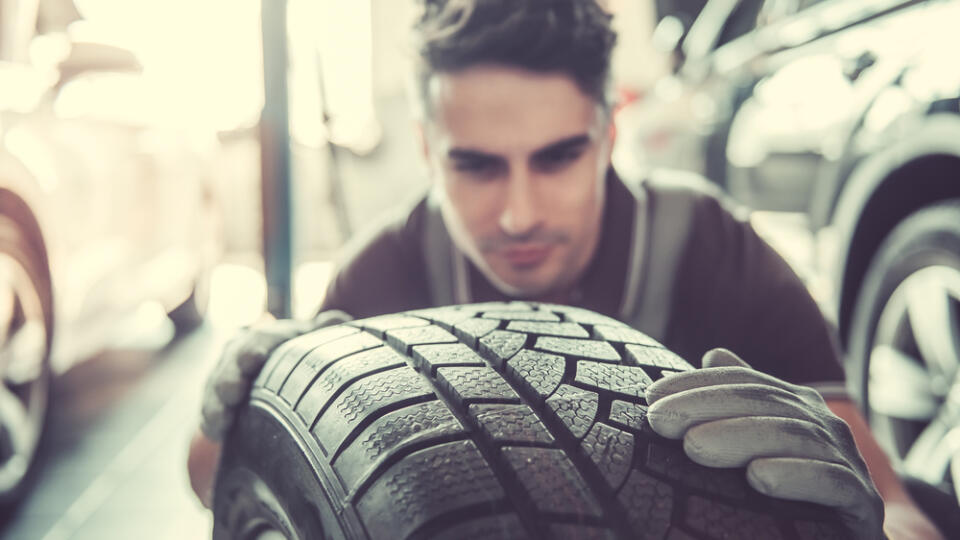 Handsome,Young,Auto,Mechanic,In,Uniform,Is,Examining,A,Tire