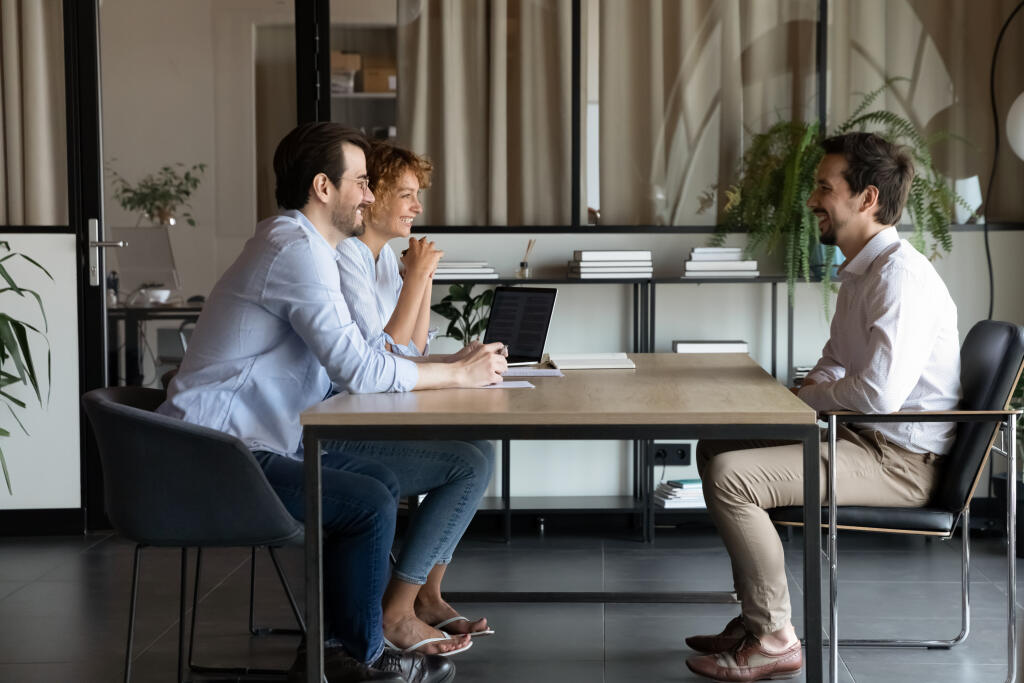 Smiling young Caucasian businesspeople talk with excited male candidate at job meeting in office. Happy man and woman recruiters speak with man applicant at interview. Recruitment, hr concept.