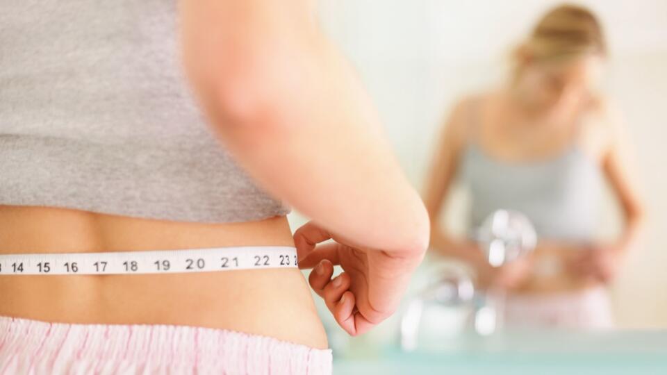 Rear view of woman measuring waist with mirror reflection