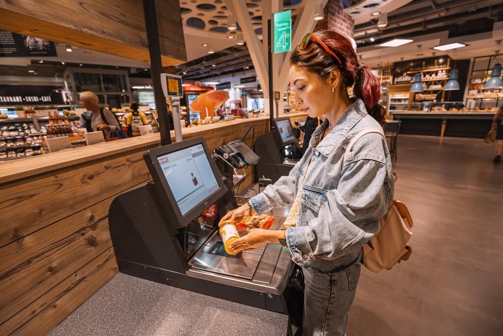 30 July 2022, Cologne, Germany: girl customer scanns and pays for bottle of juce at an automated self-service checkout terminal in Rewe supermarket