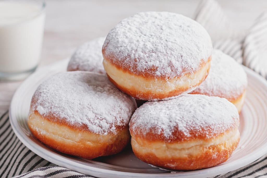 Delicious strawberry jam filled berliner doughnuts on white plate and glass of milk on wooden table top overhead