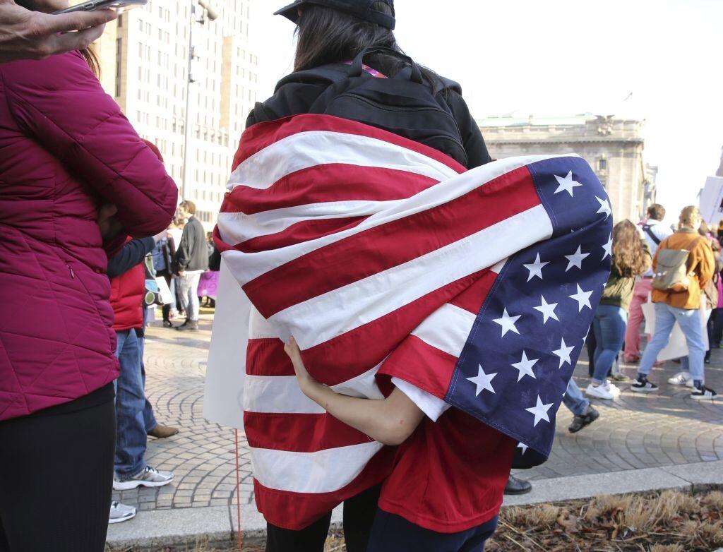 Dylan McCollum, 7, plays beneath the American flag worn upside down by his mother Nina McCollum at a Public Square rally before a Women's March on Cleveland  on Saturday, Jan. 21, 2017. The march was held in in conjunction with with similar events taking place around the nation following the inauguration of President Donald Trump   (Thomas Ondrey/The Plain Dealer via AP)