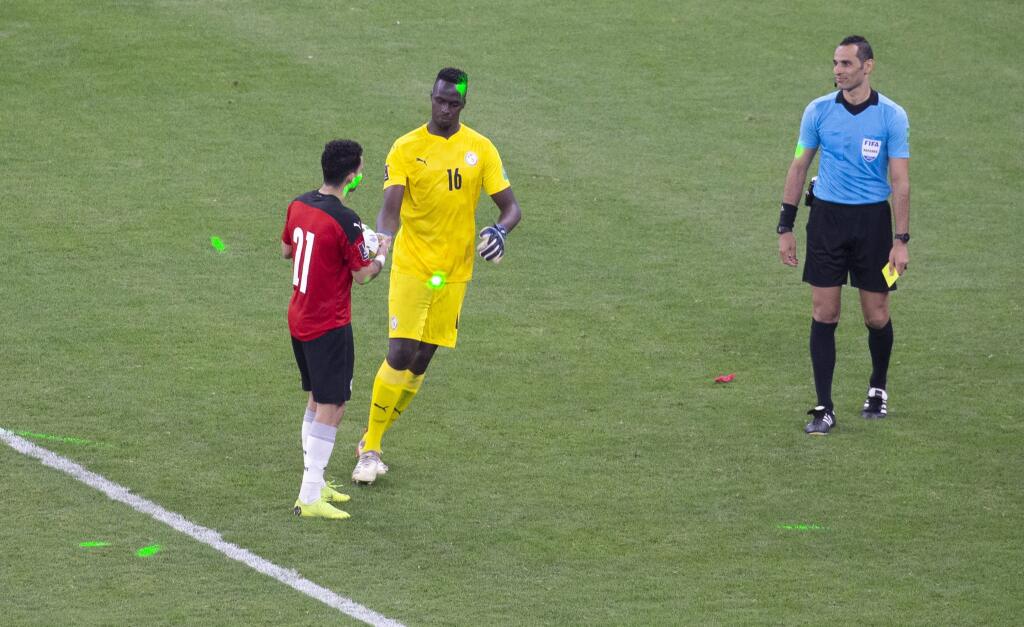 PK 9 Dakar - Na snímke zľava egyptský futbalista Ramy Rabia a brankár Senegalu Edouard Mendy sú osvetlení zelenými laserovými svetlami počas penaltového rozstrelu v odvetnom zápase play off africkej zóny kvalifikácie na MS 2022 v Katare vo futbale Senegal - Egypt v Dakare v utorok 29. marca 2022. FOTO TASR/AP
The light from green laser pointers can be seen on the pitch as Egypt's Ramy Rabia, left, shakes hand with Senegal's goalkeeper Edouard Mendy before as he prepares to take his penalty kick