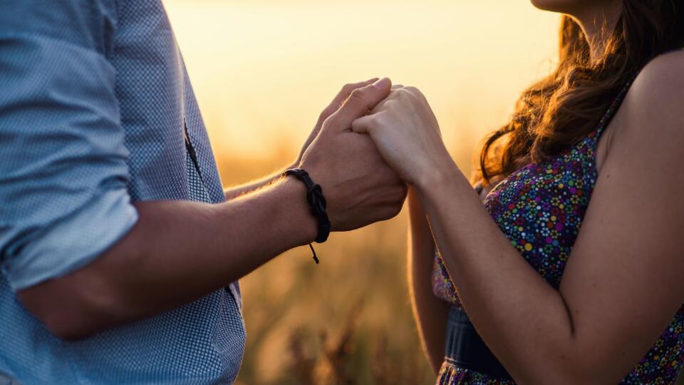 Holding hands loving couple stands in the middle of the wheat field at sunrise