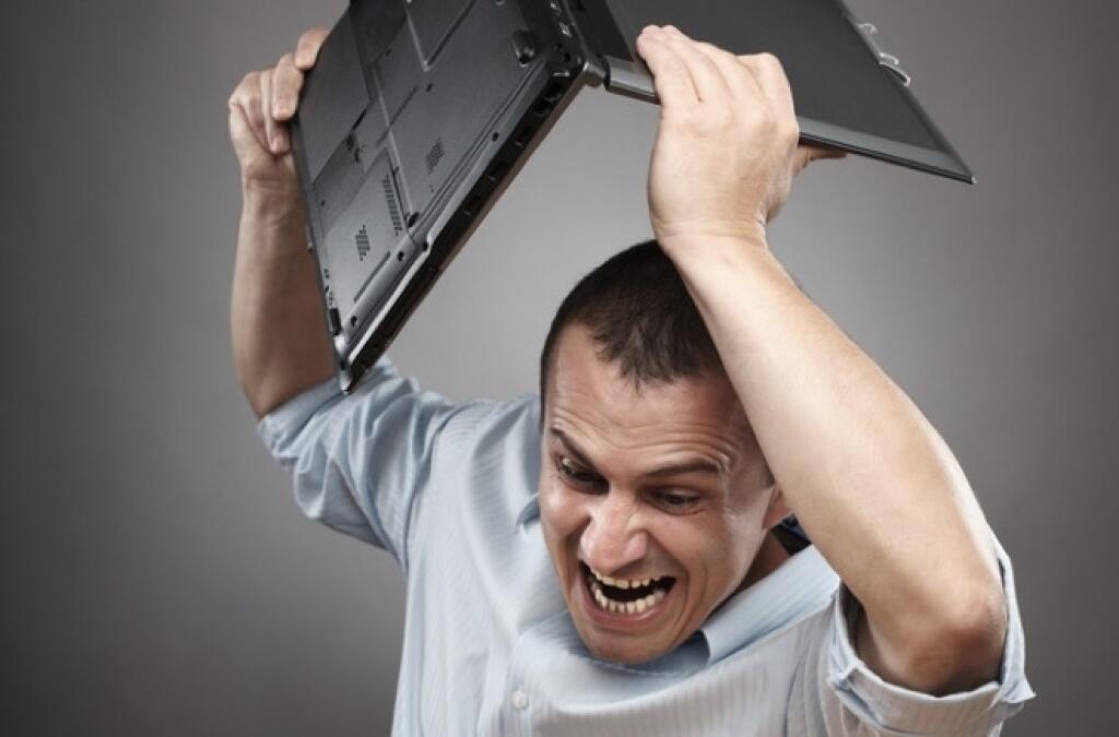 Extremely angry businessman smashing his laptop on the desk