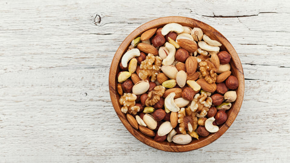 Wooden,Bowl,With,Mixed,Nuts,On,White,Table,From,Above.