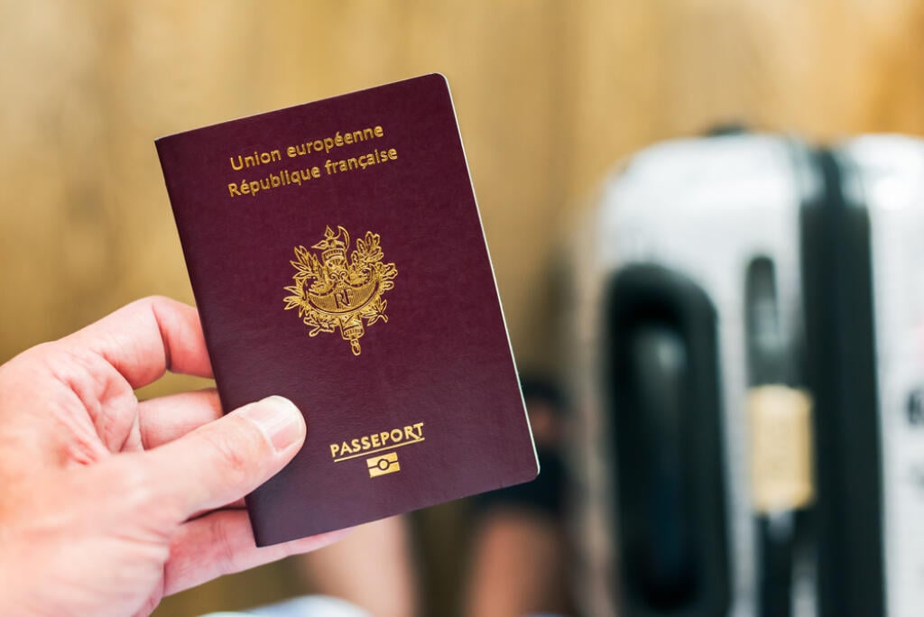 Hand holding a french - european passport with luggage in the background