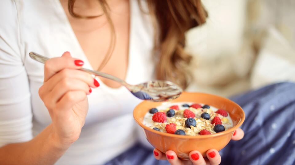 woman in pajamas in bedroom eating muesli with berries