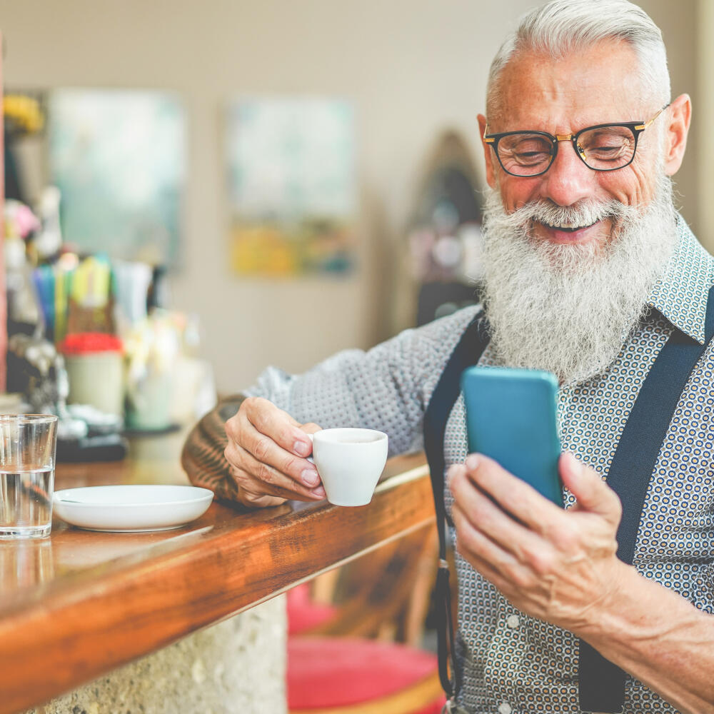 Happy,Senior,Man,Using,Smartphone,App,While,Drinking,Coffee,Inside