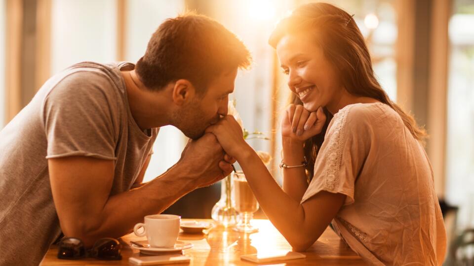 Smiling woman enjoying in a cafe while being kissed in a hand by her boyfriend.