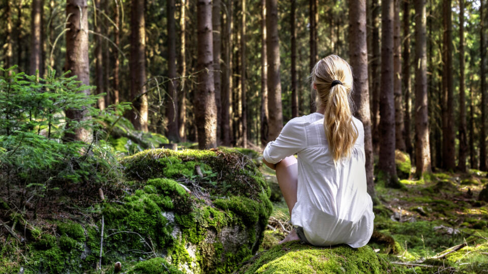 Woman sitting in green forest enjoys the silence and beauty of nature.