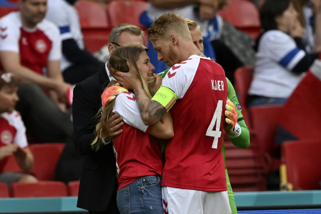 Brankár dánskej futbalovej reprezentácie Kasper Schmeichel (zelený dres) a kapitán Simon Kjaer utešujú Sabrinu Kvistovú (druhá vľavo), manželku dánskeho futbalistu Christiana Eriksena, ktorý skolaboval počas zápasu základnej B-skupiny Dánsko - Fínsko na európskom šampionáte v Kodani v sobotu 12. júna 2021.