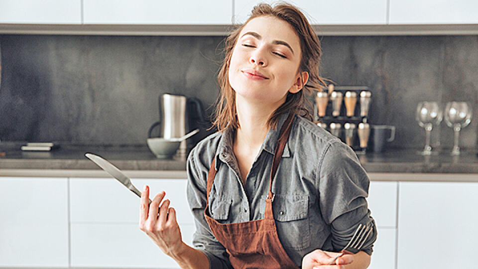 Image of pretty young woman sitting in kitchen while eating fish and tomatoes.