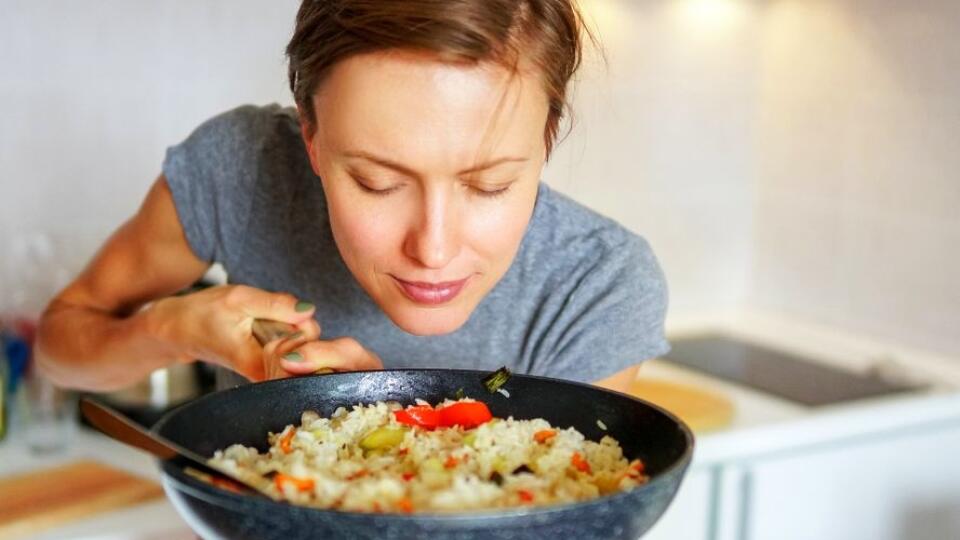 Young woman going to eat rice with vegetables, smelling delicious aroma fro just prepared food