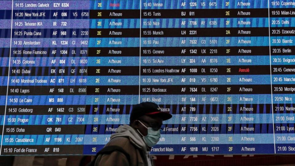 Passenger wearing a face mask walk past a flight information board at Paris' Charles de Gaulle international airport in Roissy, Monday Dec. 21, 2020