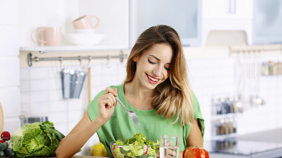 Woman eating vegetable salad at table in kitchen. Healthy diet