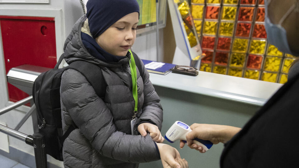 Učiteľka s ochranným rúškom na zabránenie šíreniu nového koronavírusu meria žiakovi teplotu pri vstupe do základnej školy v Moskve.