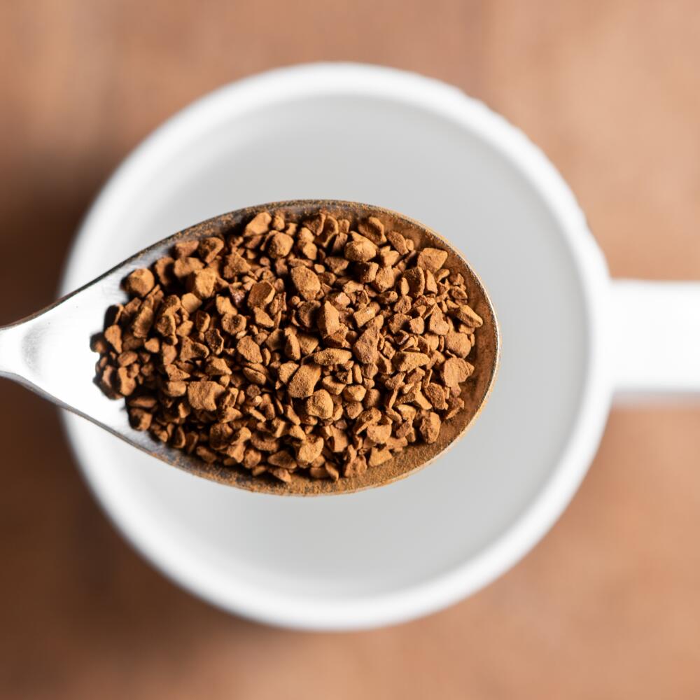 Top view of a spoon filled with instant coffee and a white cup in the background. Preparing instant coffee.