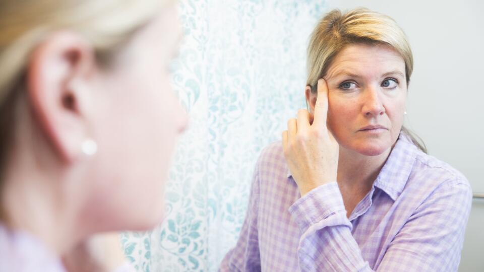 Middle-aged woman looks at her face in a mirror